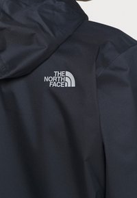 Nahaufnahme einer schwarzen The North Face Jacke, die einen Teil der Kapuze und das Logo auf dem oberen Rücken zeigt.