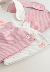 Deux bavoirs en coton côtelé pour bébé, un blanc et un rose, avec des fermetures pression, et deux bonnets en coton côtelé assortis pour bébé avec de petites oreilles d’ours.