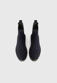 Botas Chelsea de ante marino con paneles laterales elásticos, diseño de tobillo alto y suela de goma negra texturizada. Superficie lisa sin patrones visibles.