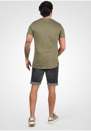 T-shirt à manches courtes vert olive avec un motif texturé, associée à un short noir retroussé et des baskets vertes.