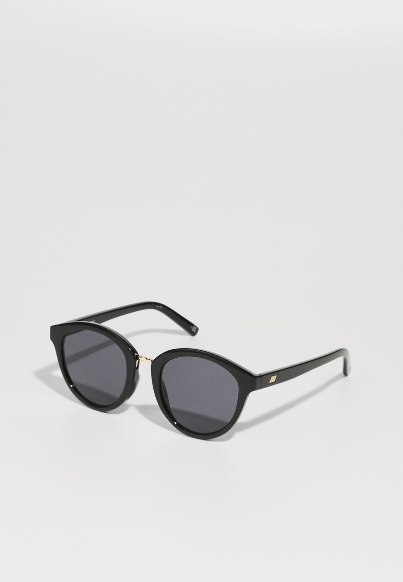 Ochelari de soare negri cu o formă îndrăzneață de tip cat-eye, având lentile întunecate și accente aurii la punte. Cadru din plastic neted cu finisaj lucios.