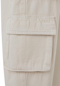 Tejido de pantalón cargo beige con un gran bolsillo lateral con solapa, costuras reforzadas y una textura diagonal.