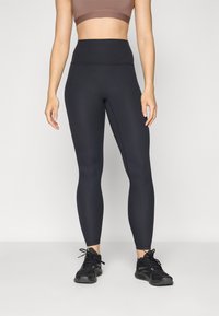 Leggings en maille côtelée taille haute de couleur bleu marine foncé. Fabriqués en matériau extensible avec une texture lisse, associés à des chaussures de sport noires.