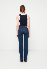 Mørkeblå, rette jeans med høy midje og en brun skinnlapp bak. Kombinert med en marineblå tanktop med hvit kant.