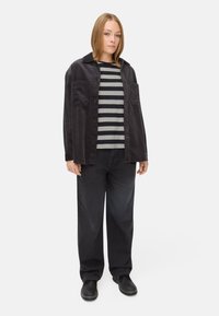 Schwarze Cordjacke, graues und schwarzes gestreiftes Langarmshirt darunter, schwarze weit geschnittene Jeans und dunkle Schuhe. Einfaches und lässiges Design.