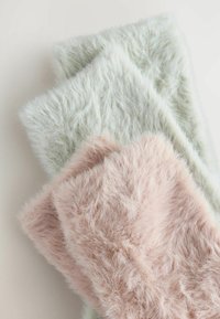 Drie pluizige plaids in pastelkleuren: één lichtgroen, één lichtroze en één zacht beige, met lange, gestructureerde vezels.