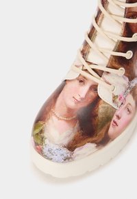 Geprinte enkelboot met een glanzende afwerking, voorzien van een ontwerp van twee vrouwengezichten. Crèmekleurige veters en een stevige witte zool.