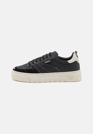 Sneaker nera con un design in materiali misti, che include pelle liscia e dettagli testurizzati. Presenta motivi a strisce bianche e una suola crema.
