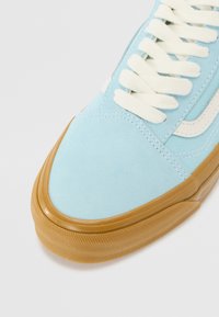 Light blue suede sneaker with cream laces, rubber tan sole, and white side stripe. Smooth texture with visible stitching details.