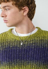 Gebreide trui met groene en paarse strepen, met een ronde hals en een textuurstof. Zilveren ketting met een kleine hangslotpendant.