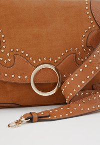 Hnědá semišová kabelka se zlatými hroty a kulatým zlatým kováním. Obsahuje vzorovaný design a odnímatelný popruh.