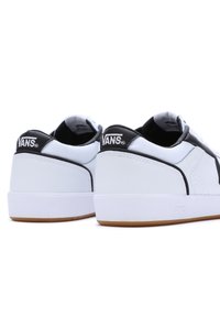 Weiße und schwarze Vans-Sneaker mit einem glatten Leder- und Stofffinish, ausgestattet mit einer Gummisohle und einem Logo an der Ferse.