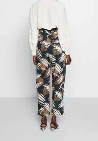 Högmidjade, vida byxor med ett tropiskt bladmönster i beige och brunt mot en mörkblå bakgrund. Slät tygtextur.