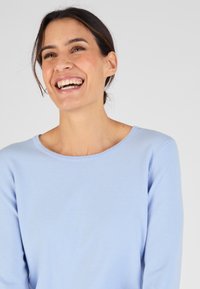 Lichtblauwe trui met een ronde hals en lange mouwen, gemaakt van zacht, fijn gebreid materiaal. Soepele textuur met subtiele stiksels.