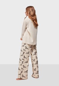 Top de manga larga beige combinado con pantalones de pijama de pierna ancha con estampado de cebra. Tejido suave, corte relajado y paleta de colores neutros.