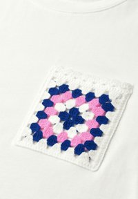 Tissu blanc avec une poche carrée au crochet avec du fil bleu marine, rose et blanc dans un motif géométrique.