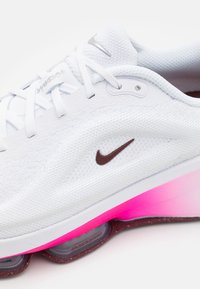Chaussure de course Nike blanche en tissu mesh respirant, logo swoosh marron, lacets blancs et semelle dégradée rose avec amorti air visible.