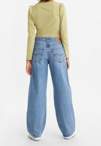 Grön rutmönstrad långärmad topp och högmidjade ljusblå vida jeans med bakfickdesign och märkesläderpatch.