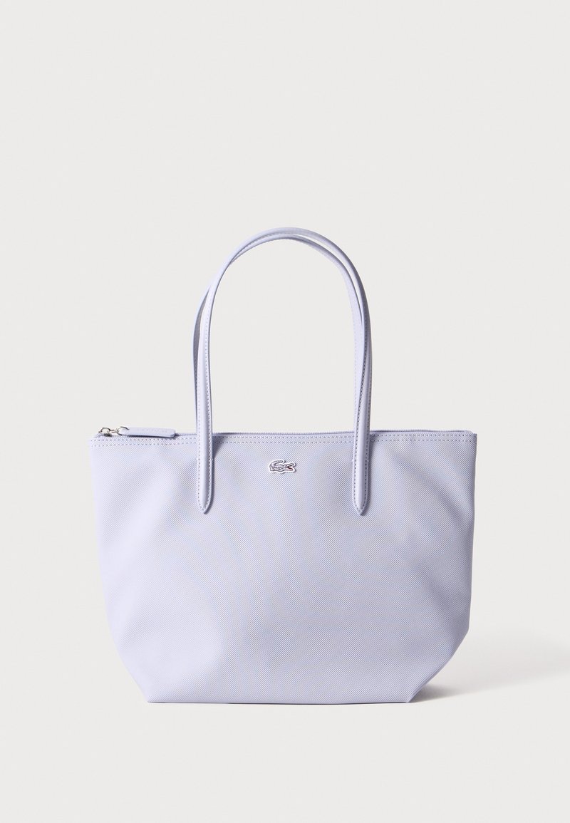 Sac cabas violet clair avec doubles poignées, petit logo brodé sur le devant et fermeture éclair sur fond uni.