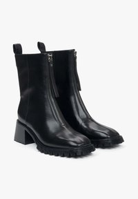 Black leather ankle boots with two side zippers, textured rubber sole, block heel, and pull tabs for easy wear. Smooth and sleek finish.