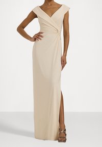 Beige bezramenné zavinovací šaty s hlubokým V-výstřihem, bočním rozparkem a nashromážděnými detaily v pase, nošené s metalickými platformovými sandály.