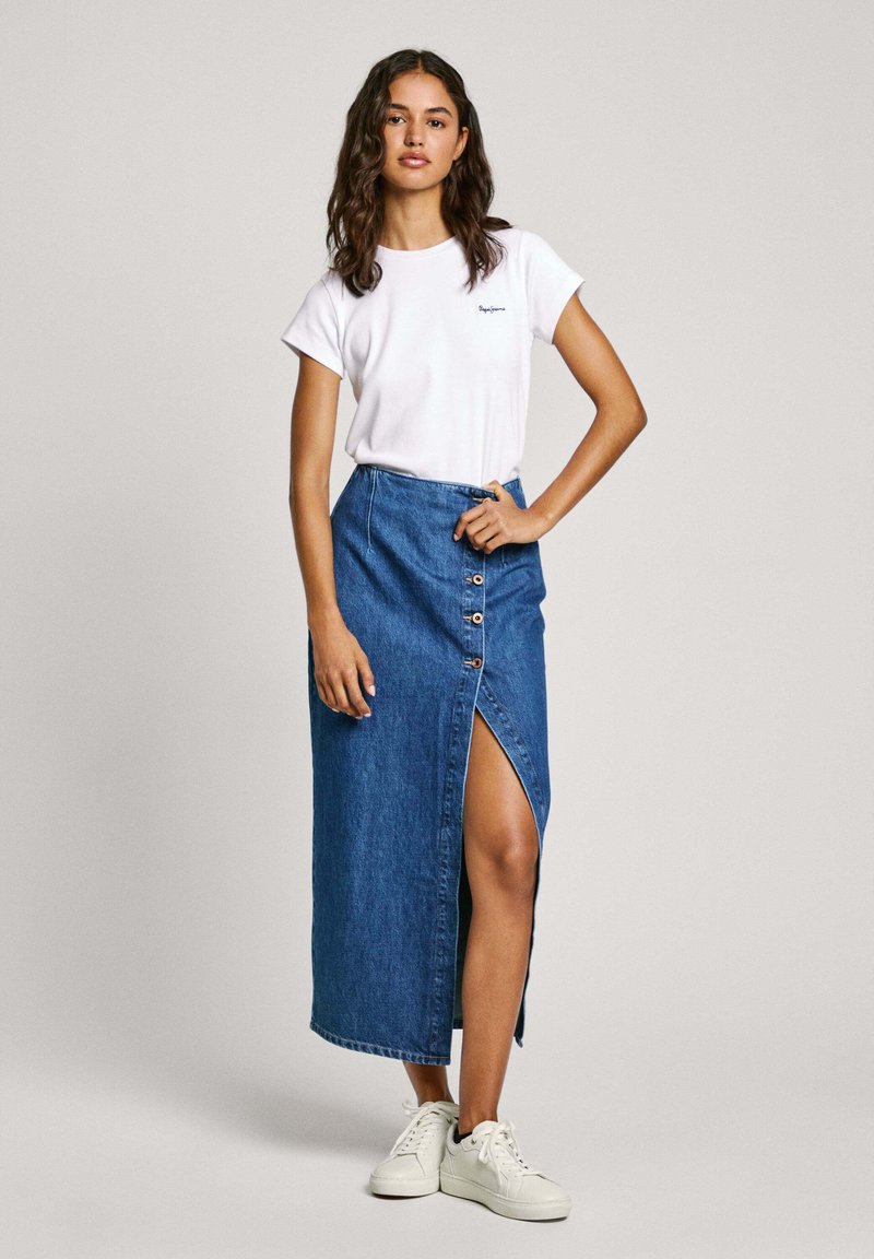 Vit kortärmad t-shirt med en liten logotyp, kombinerad med en lång denimkjol med slits fram och knappeffekter, buren med vita sneakers.