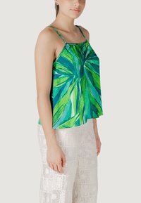 Top sin mangas con diseño de hojas tropicales verdes y un corte fluido. La tela es ligera, combinada con pantalones blancos texturizados.