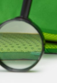 Svart förstoringsglas över texturerad grön tyg med cirkulära mönster, som visar en slät yta och livfulla färger mot en suddig bakgrund.
