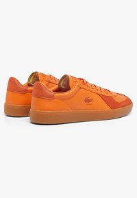 Baskets en cuir orange avec un panneau en daim texturé, des lacets plats et une semelle en caoutchouc. Logo embossé sur le talon.
