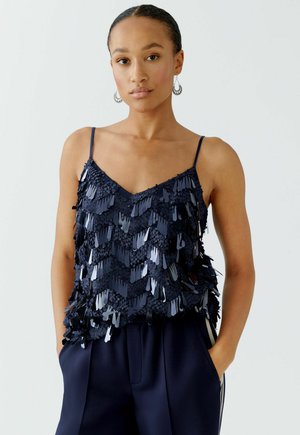 Navy blue tank top with shimmering fringe detailing. Adjustable spaghetti straps and a V-neck design. Soft, textured material.