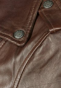 Nahaufnahme einer braunen Lederjacke mit glatter Textur, silbernen Knöpfen und sichtbaren Nähten entlang der Sch seams und des Kragens.