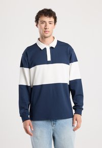 Long-sleeve polo shirt featuring navy and white horizontal stripes, a buttoned collar, and soft, textured fabric. Classic fit design.