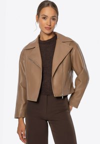 Tan leren cropped jack met een kentkraag, rits aan de voorkant en zijzakken, gecombineerd met een donkere trui en bruine broek.