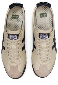 Beige leather sneakers with dark blue accents, textured taupe suede toe cap, and white mesh lining. Features flat laces and logo patches.
