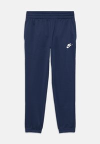 Jūras zila Nike sporta bikses ar elastīgu jostu, sašaurinātiem dibeniem un baltu Swoosh logo augšējā kreisajā pusē. Gluda auduma tekstūra.