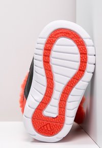 Podeszwa sneakersów Adidas z białą podstawą i czerwonym wzorem przyczepności, zaokrąglony kształt i wyściełana faktura. Widoczny element zapobiegający poślizgowi.