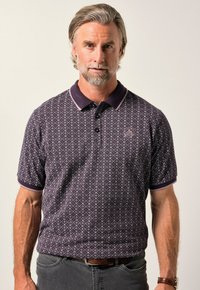 Mörk lila polo skjorta med ett geometriskt mönster, med en kontrasterande krage och manschetter i ljusare lila. Korta ärmar och två knappar.