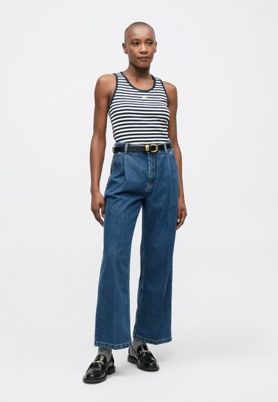 Stripete ermeløs tanktop med rund hals, paret med høyt liv blå denim vide bukser og svarte loafers med gull detaljer.