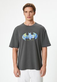 Camiseta de algod�ón gris con mangas cortas que presenta un diseño del logo de Batman en azul y amarillo en el centro, cuello reforzado y un corte relajado.
