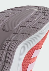 Podeszwa buta sportowego z teksturowaną, elastyczną fioletową środkową warstwą gumową, białym obramowaniem i żywą czerwoną cholewką z plecionym wzorem oraz różowymi akcentami.