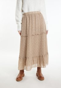Vloeiende, gelaagde maxi-rok in beige bloemenprint, met een elastische tailleband en ruches aan de randen, gecombineerd met bruine enkellaarsjes.