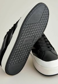 Mustad mustad mustad ja tekstuurse kummist tallaga, suede aktsentidega ja valge vahega. Omab musti paelu ja logo külgkolle.