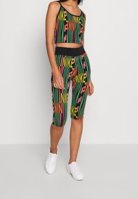 Kolorowy zestaw odzieży sportowej z czarnym topem w formie crop i legginsami do kolan z odważnymi różowymi, zielonymi i żółtymi logo oraz paskami Nike.