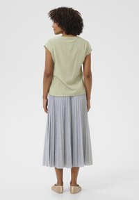 Top corto verde chiaro a maniche corte con finitura testurizzata, abbinato a una lunga gonna grigia plissettata con sottili righe. Scarpe marroni completano l'outfit.