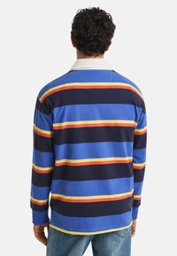 Langermet polo-shirt med blå, marineblå og stripete mønstre med røde, gule og oransje detaljer. Krage-design. Behagelig strikket materiale.