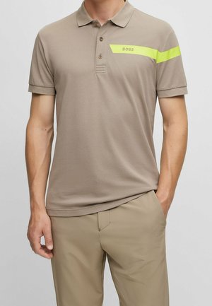 Beige poloshirt met drie knopen, korte mouwen en een horizontale gele streep met de tekst "BOSS" op de borst, gedragen met bijpassende beige broek.