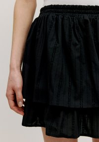 Zwarte gelaagde rok van textuurstof met een elastische tailleband. Bevat verticale strepen voor extra detail en een gelaagd ontwerp.