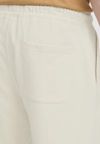 Cream-colored sweatpants made of soft cotton, featuring an elastic waistband and a single back pocket with a stitched edge detail.