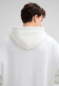 Witte hoodie met een grote, gewatteerde kraag, ontworpen met een textuurstof. Heeft een ontspannen pasvorm en zichtbare stiksel details bij de nek.