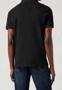 Czarna koszulka polo z krótkim rękawem, gładka w dotyku, z zapięciem na dwa guziki i luźnym krojem, połączona z ciemnoniebieskimi dżinsami.